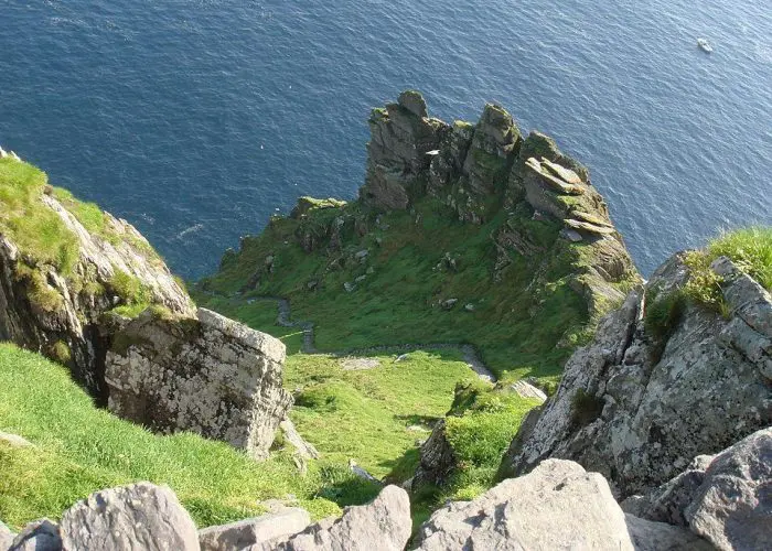 A rugged cliffside with green grass overlooking a deep blue sea.