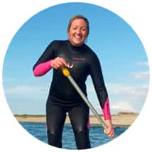 Woman in wetsuit paddleboarding on water.