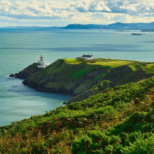 A picturesque lighthouse on a coastal headland overlooking the sea, under a partly cloudy sky.