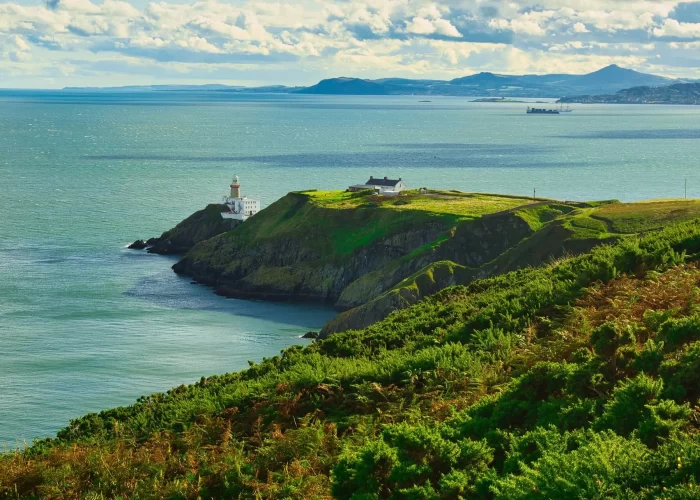 A picturesque lighthouse on a coastal headland overlooking the sea, under a partly cloudy sky.