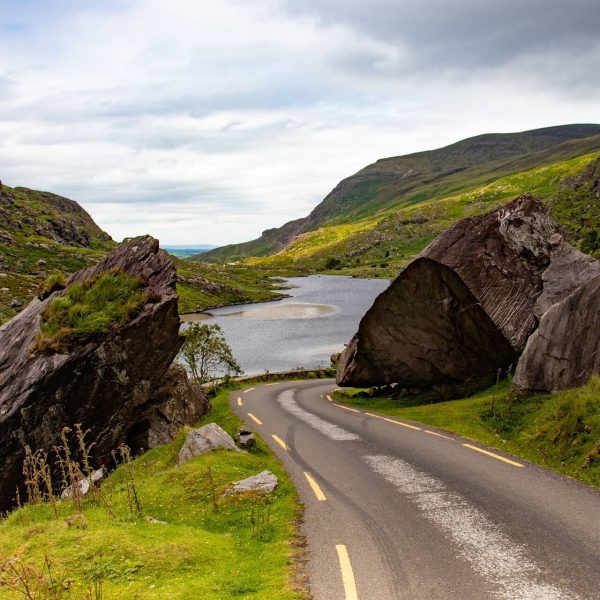 A winding road through a hilly landscape with large boulders and a river.