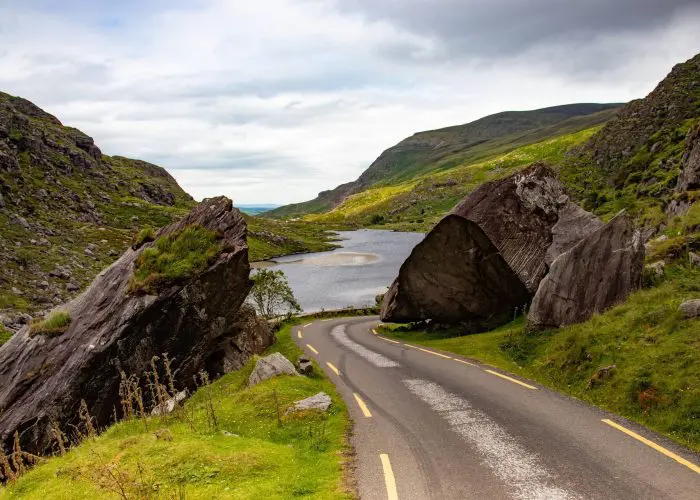 A winding road through a hilly landscape with large boulders and a river.
