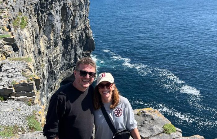 A couple posing for a photo on a coastal cliff under clear skies in Ireland.