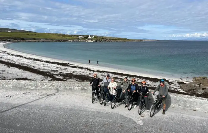 Group of cyclists posing in front of a scenic beach landscape with clear skies on a Private Tour.