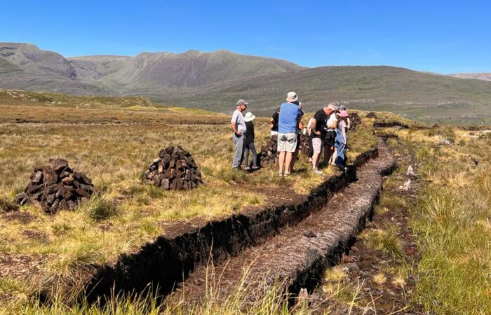 Group of people on a Small Group Tour examining a peat bog in Ireland with cut peat in the foreground and mountains in the distance.