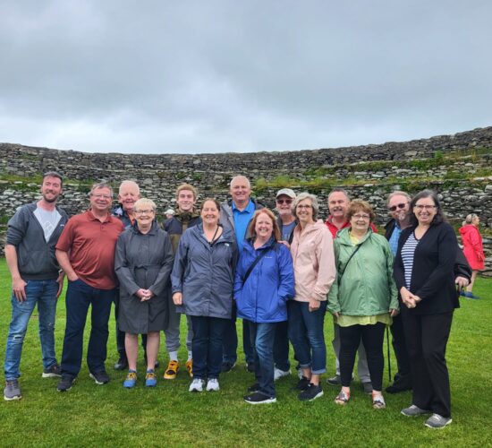 A small group of people posing for a photo in front of historic stone ruins on a cloudy day.