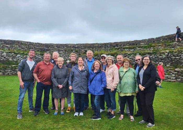 A group of adults posing for a photo in front of ancient stone ruins under an overcast sky.