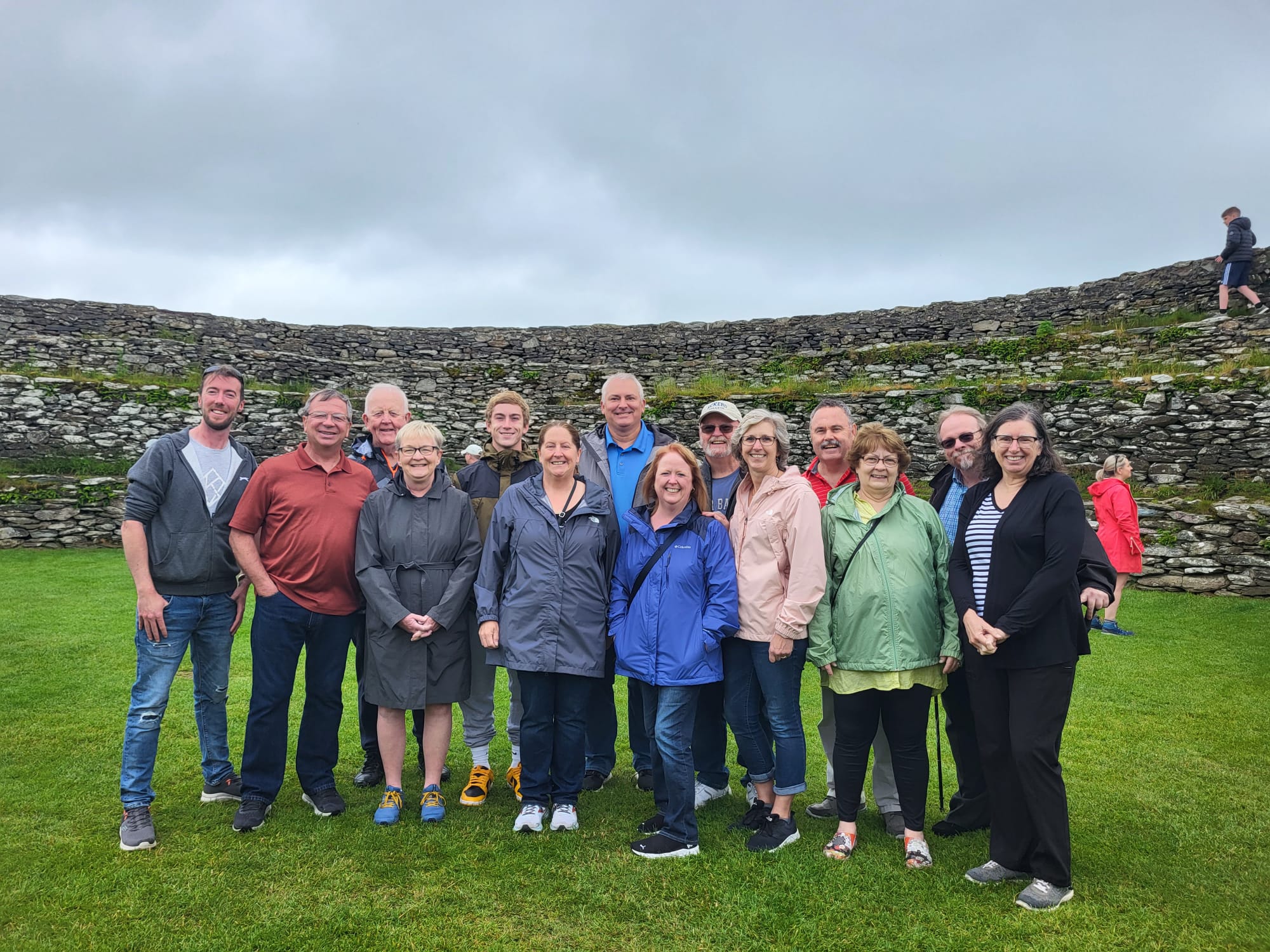 A small group of people posing for a photo in front of historic stone ruins on a cloudy day.