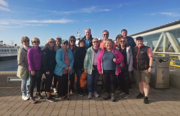 A group of tourists posing for a photo at a harbor in Ireland on a sunny day.