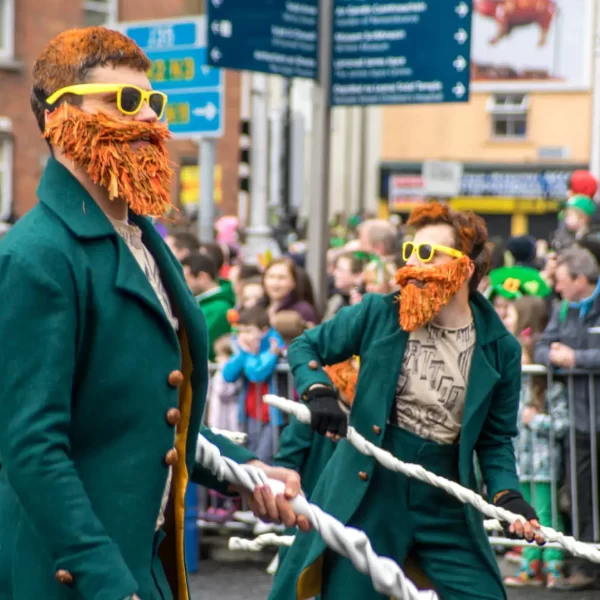 Participants in vibrant green costumes with orange beards march in a st. patrick's day parade.