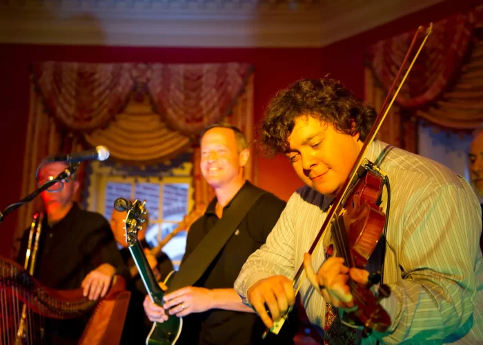A group of musicians performing, featuring a violinist in the foreground.