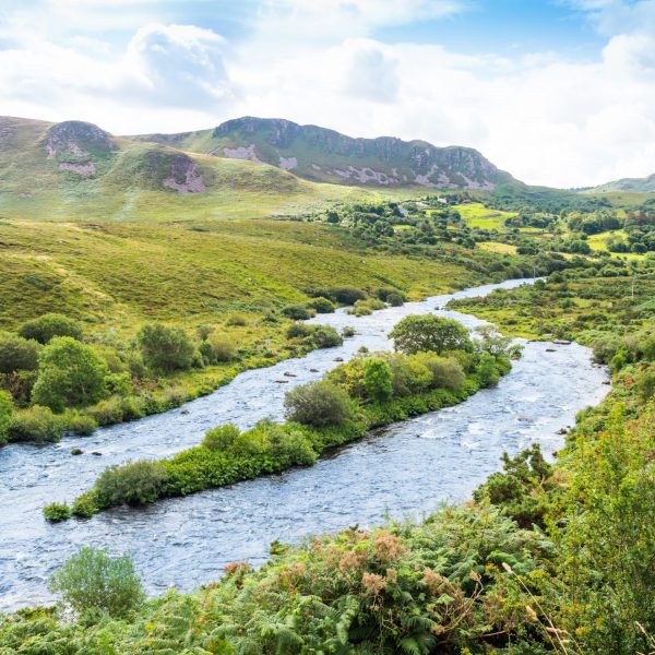 A serene river meandering through a lush, hilly landscape under a bright blue sky with clouds.