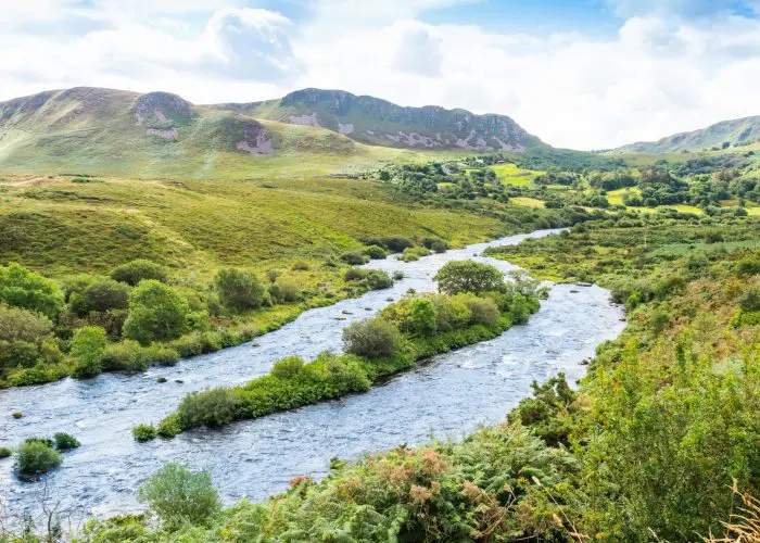 A serene river meandering through a lush, hilly landscape under a bright blue sky with clouds.