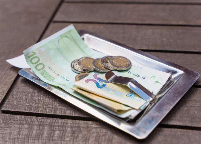 A bill with cash and coins on a tray indicating a payment or a tip left on a wooden table.