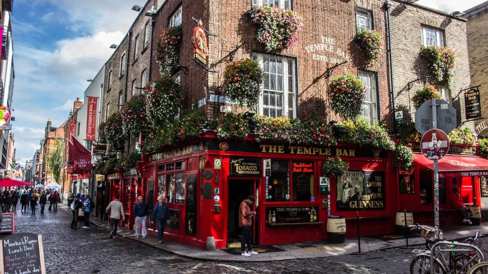 A bustling street view of the iconic temple bar pub adorned with vibrant flower baskets in dublin, ireland.