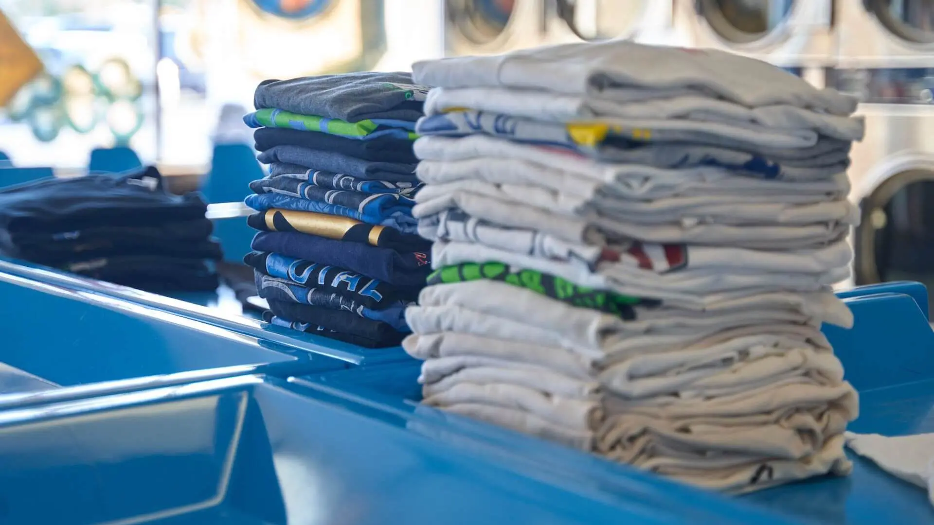 Neatly folded clothing stacks on a laundromat folding table.