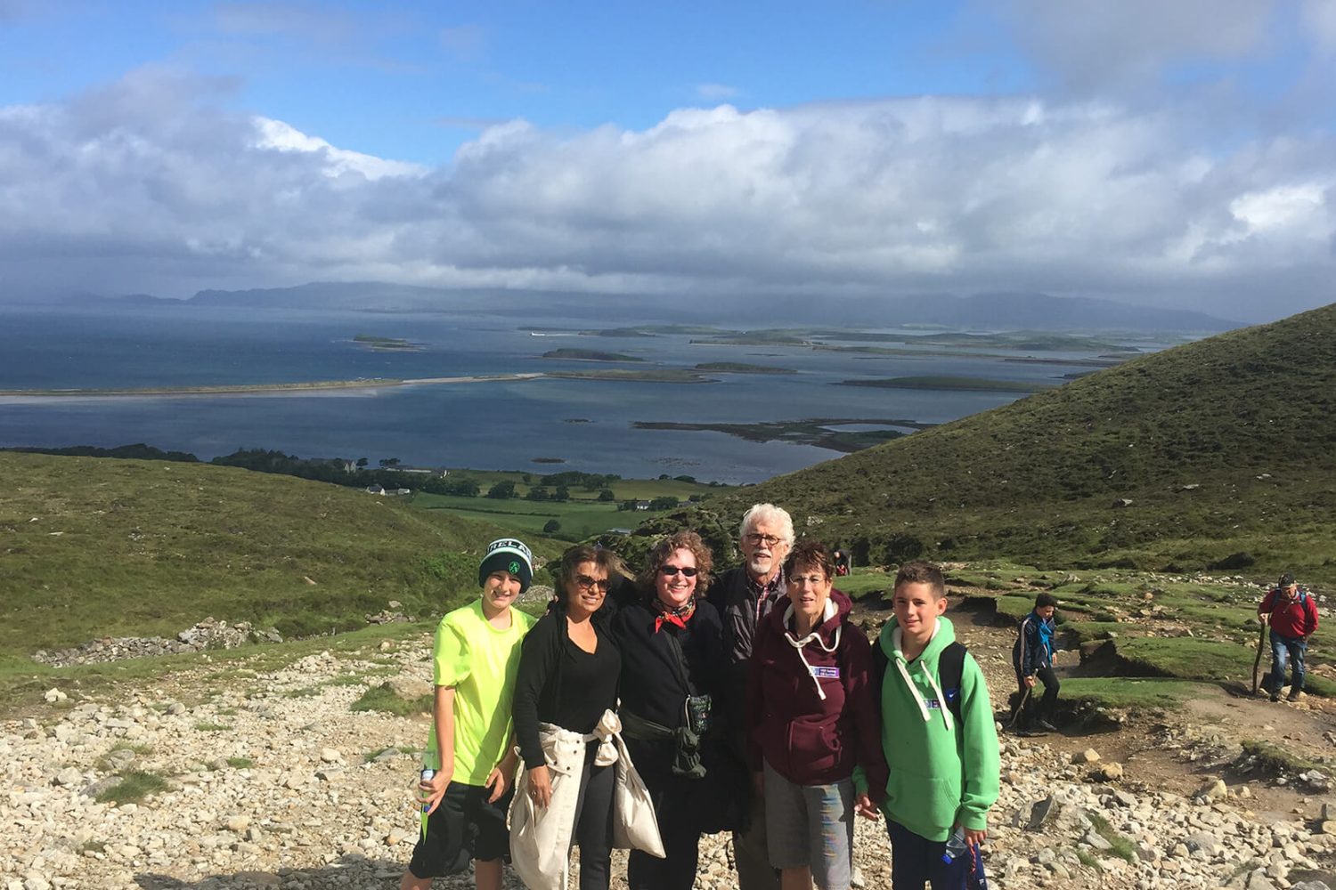 Group of hikers posing for a photo with a scenic bay and rolling hills in the background of Ireland.
