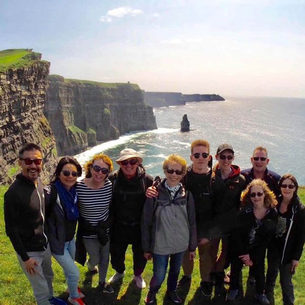 Group of tourists posing for a photo at the cliffs of moher in ireland.