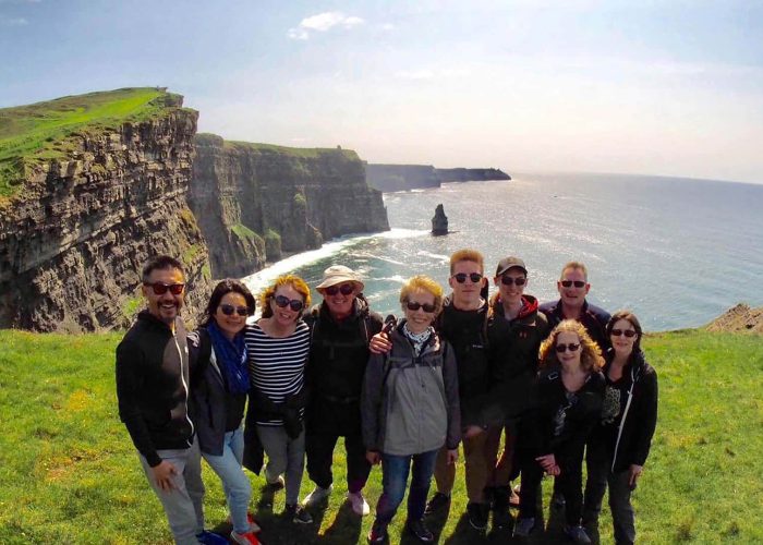 Group of tourists posing for a photo at the cliffs of moher in ireland.