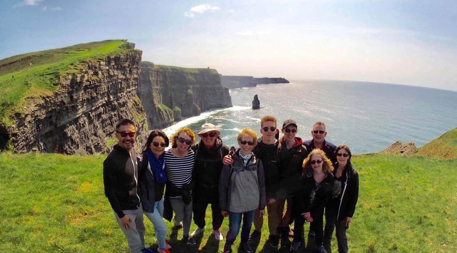 Group of tourists posing for a photo at the cliffs of moher in ireland.