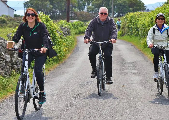 Three adults cycling on a rural road with smiles.