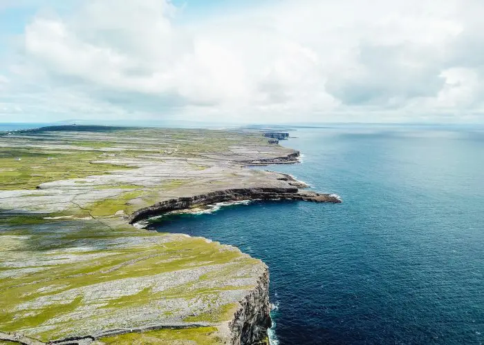 Aerial view of a rugged coastline with cliffs overlooking the ocean under a partly cloudy sky.