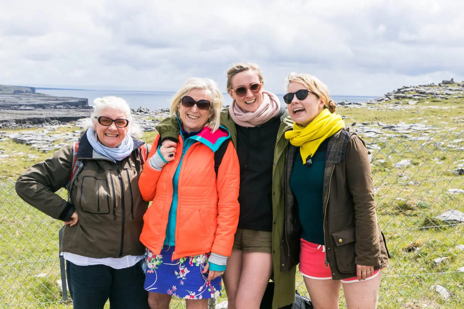 Four women smiling together in an outdoor setting with rocky terrain in Ireland in the background.