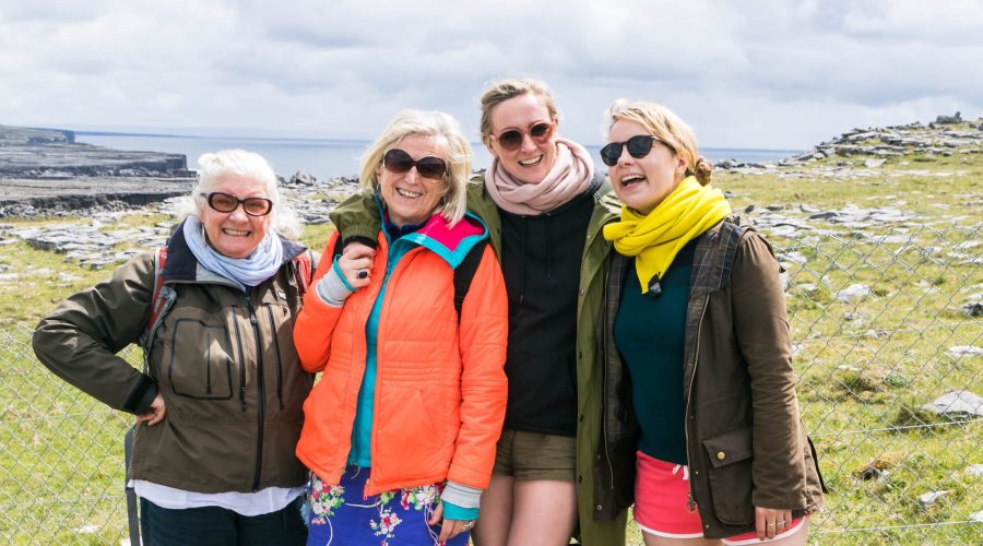 Four smiling women posing together outdoors on a sunny day with a rocky landscape in the background.