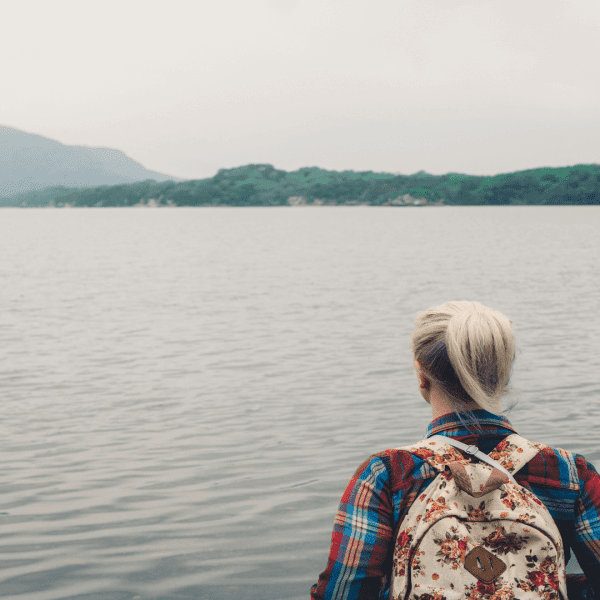 Woman with a backpack standing by the lake looking at the view.