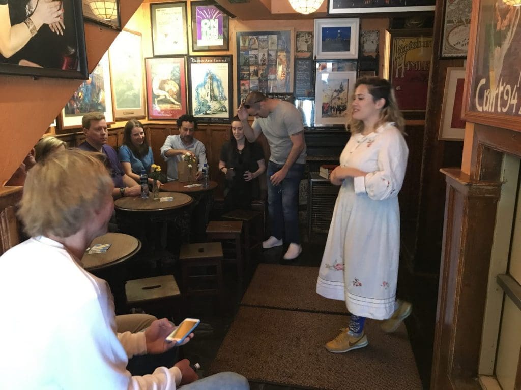 A woman in traditional dress singing to a group of people in a cozy pub with posters and decor on the walls.