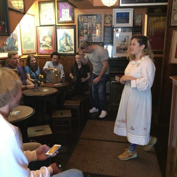 A woman in traditional dress singing to a group of people in a cozy pub with posters and decor on the walls.