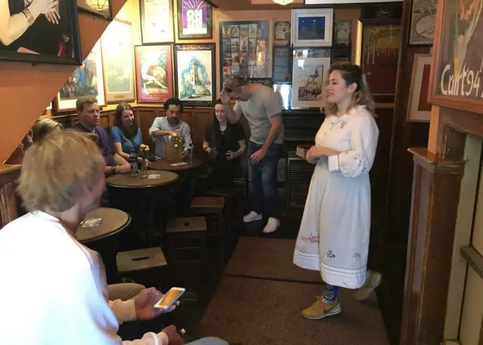 A woman in traditional dress singing to a group of people in a cozy pub with posters and decor on the walls.