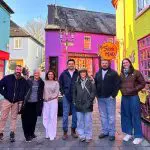 A group of seven people standing on a colorful street with brightly painted buildings, including a purple one and a yellow one, posing for a photo. A person is seen walking on the side, capturing the lively spirit of activity holidays in Ireland.