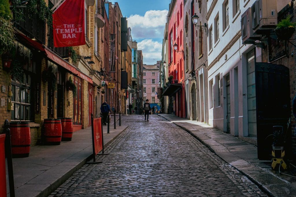 Cobbled street in temple bar, dublin, with colorful buildings and people walking under a clear sky.