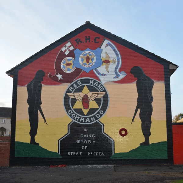 Mural on a building wall memorializing "stevie mccrea," featuring images of masked figures, military emblems, and the red hand commando logo.