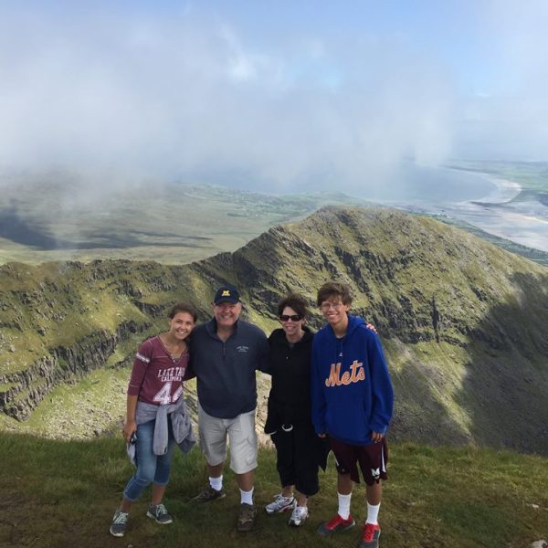 Four people posing on a mountain summit with a misty valley and rugged hills in the background.