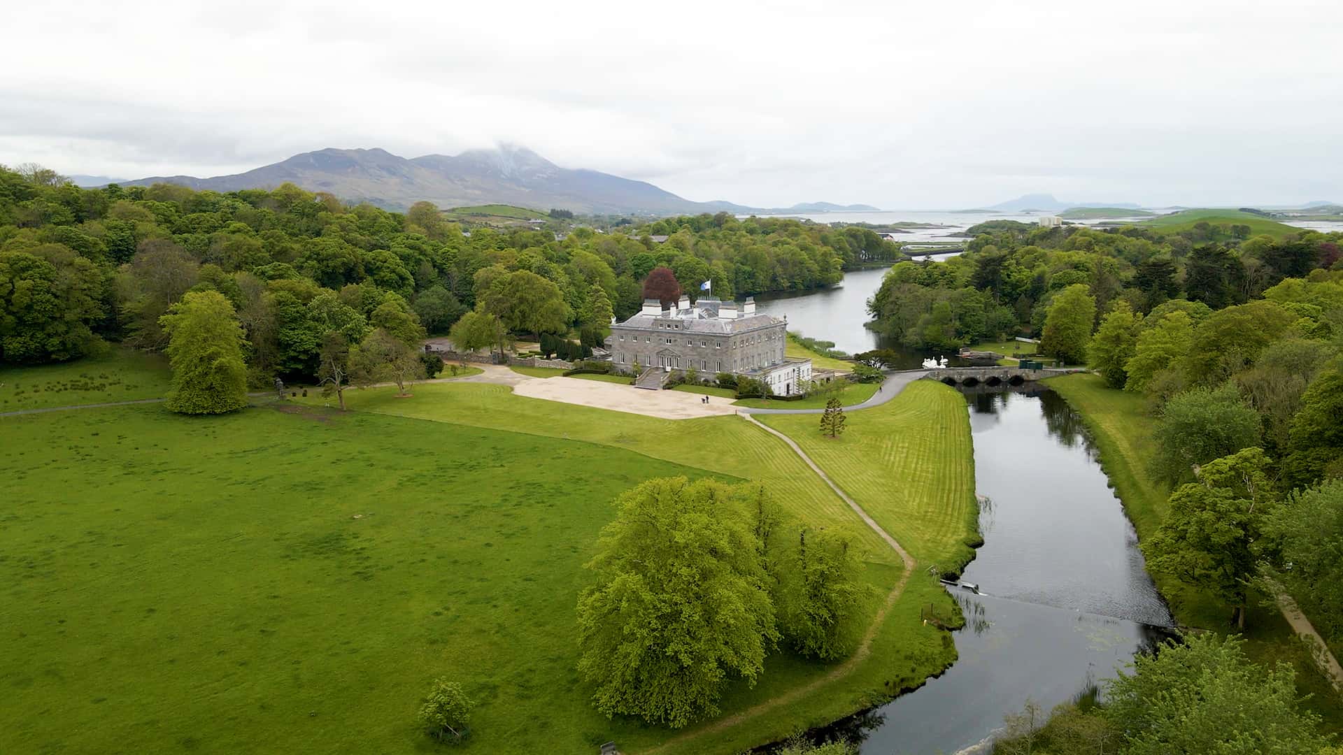 Aerial view of a large estate surrounded by lush greenery and a river, with mountains visible in the background, perfect for tailor-made tours.