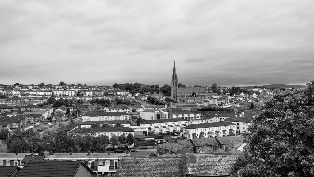 Black and white photo of a town with tightly packed houses, a prominent church spire, and a cloudy sky.