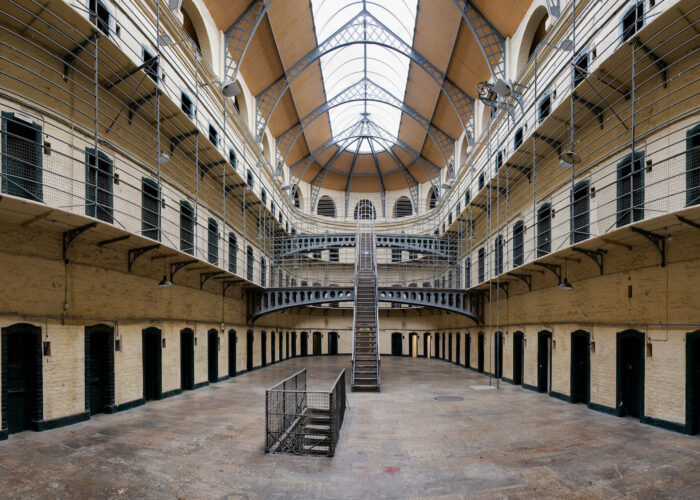 The interior of this famous historic prison wing in Ireland features multiple levels, barred cell doors, and a staircase leading to an upper walkway beneath a high arched ceiling. Known also as one of the country's supernatural sites, it offers an eerie glimpse into the past.